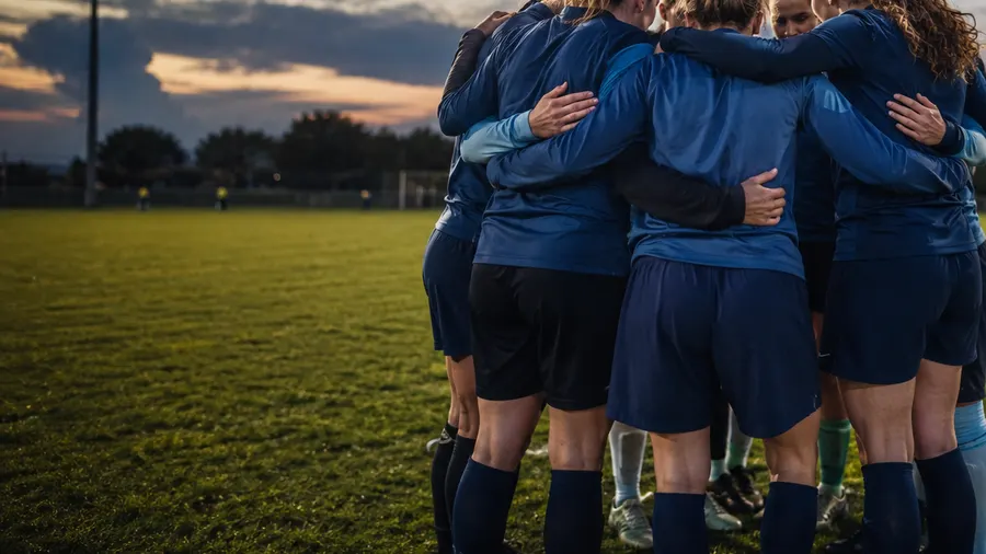 A team huddle under floodlights at dusk.